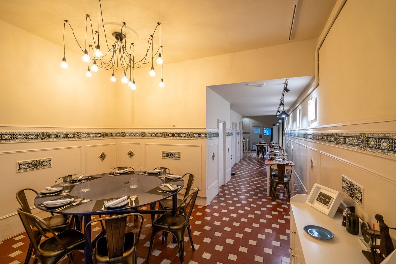 The dining room at Avenir, a round table under a bare-bulb chandelier, tiled floors running back