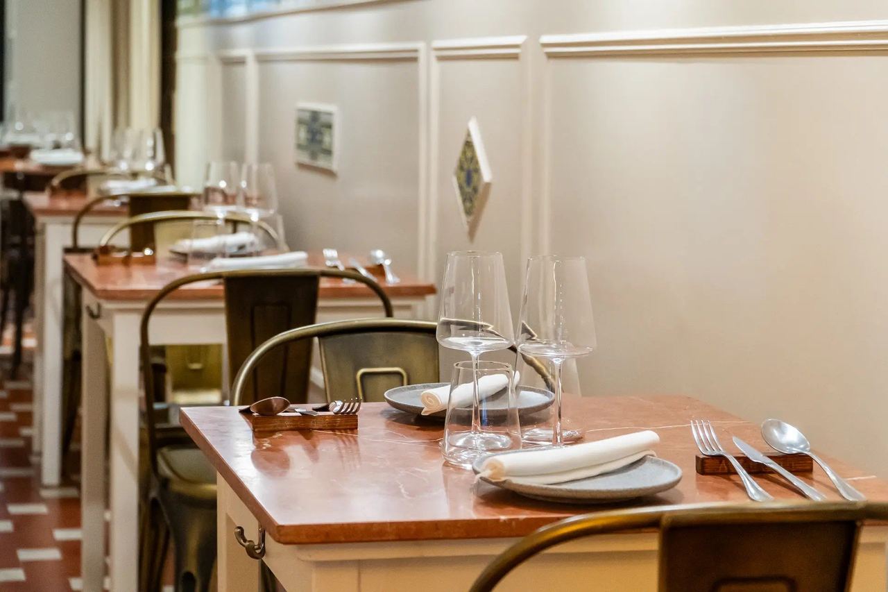 Tables laid with red marble tops and metal chairs along the panelled wall at Avenir
