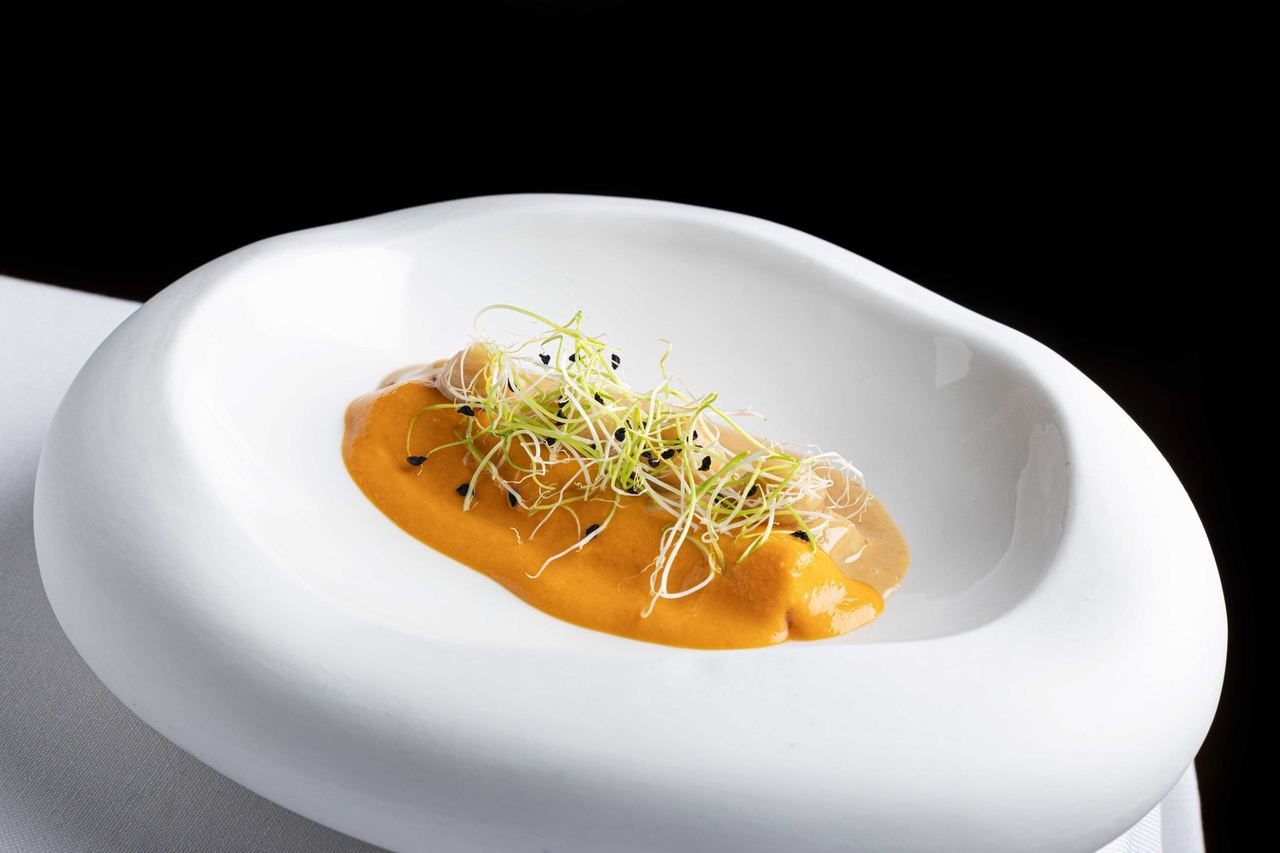 A dish of seafood under a bright orange sauce and sprouts at Hofmann