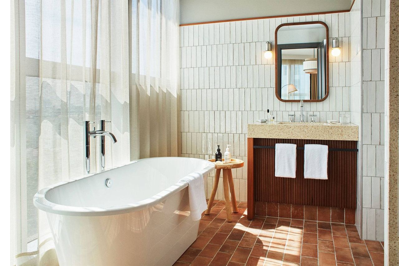 A bathroom at The Hoxton, Poblenou, with a freestanding tub, white tiles and terracotta floor