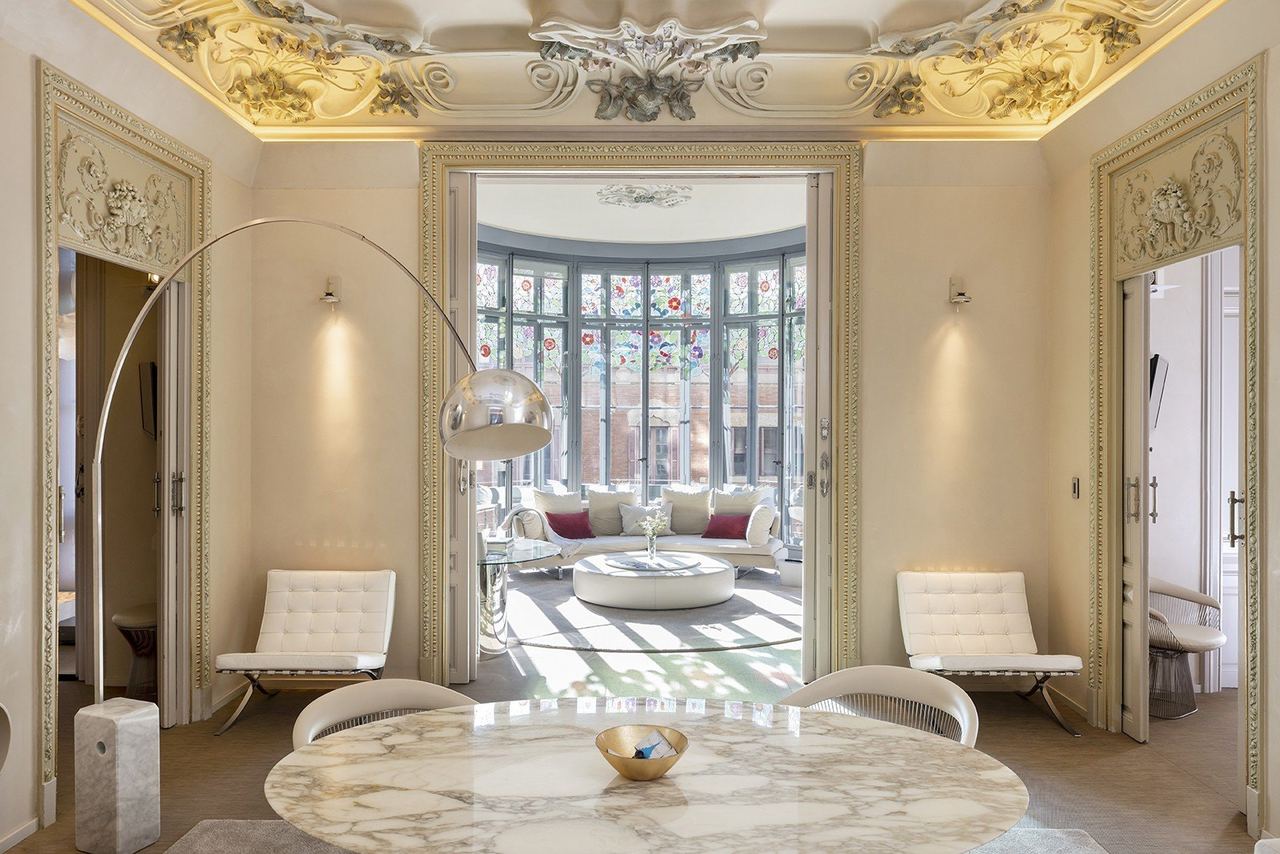 A suite at El Palauet, white chairs under a Modernista plaster ceiling, a stained-glass gallery beyond