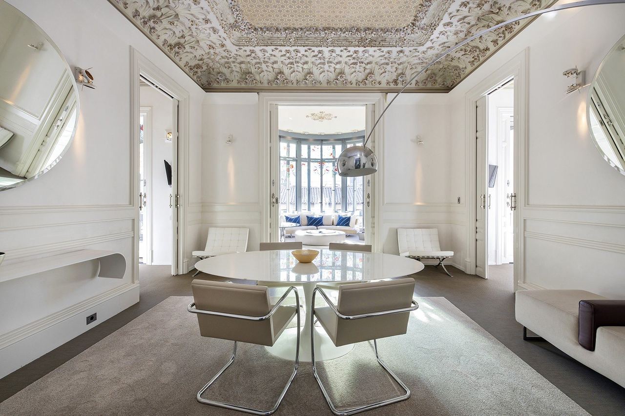 A dining salon at El Palauet under a painted ceiling, opening onto a glazed gallery