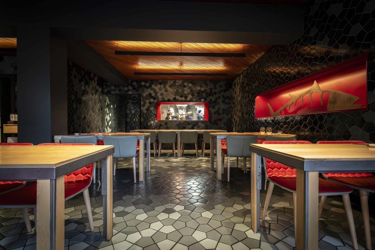 The dining room at Tunateca Balfegó, red chairs on a mosaic floor, a bronze tuna on a red panel