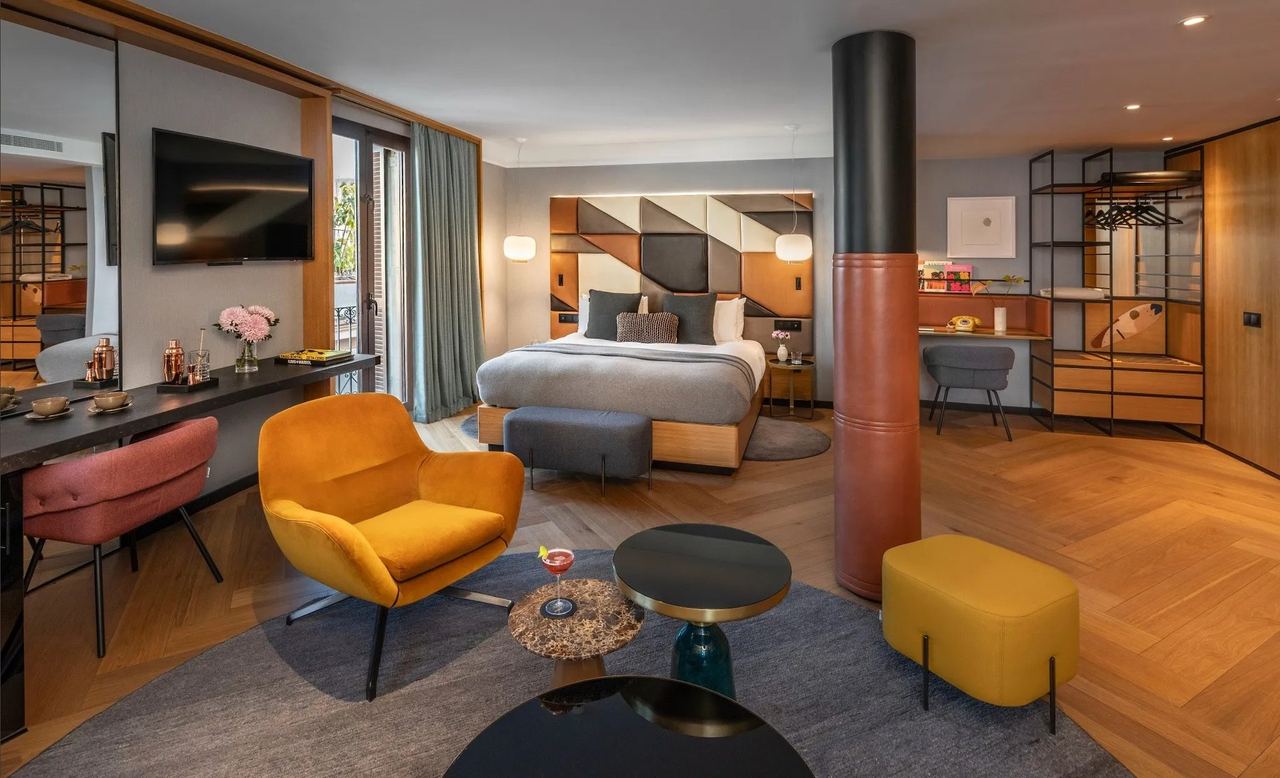 A suite at Kimpton Vividora, a mustard armchair and herringbone floor before the bed